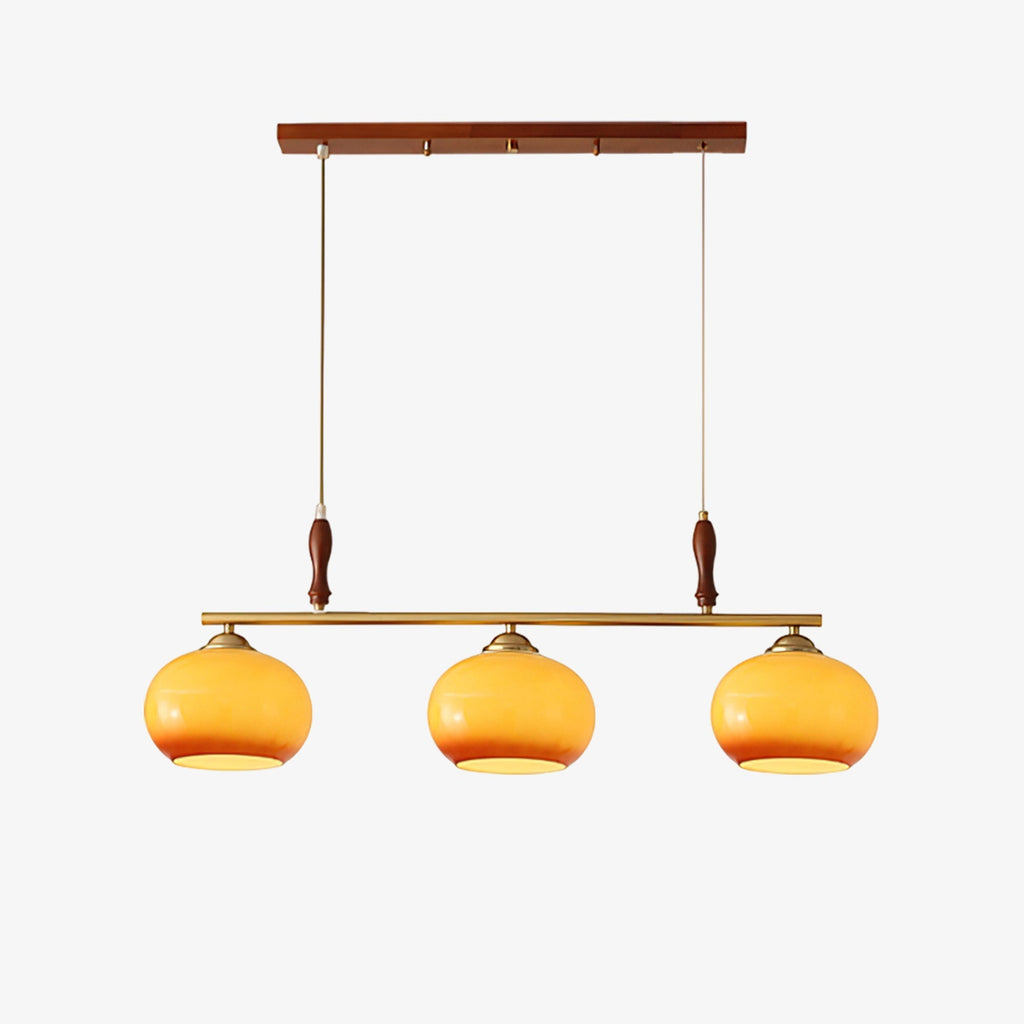 This Clérachic three-head bar pendant on a plain light backdrop, with amber glass shades, a brass bar and walnut-toned wooden accents.