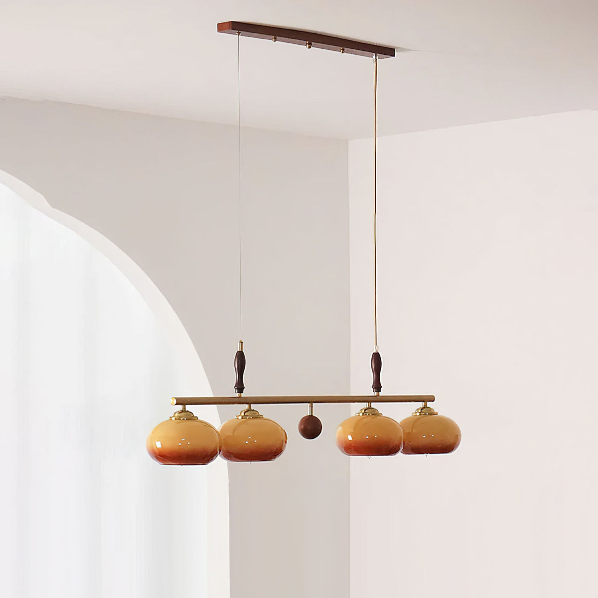 Four-head Clérachic bar pendant with a wooden ball at its centre, hung from a wooden ceiling plate in front of an arched white wall.