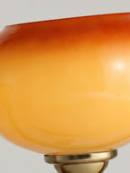 Close view of the glossy glass of a Clérachic shade, shading from golden yellow to deep orange, with the brass cap just visible below.