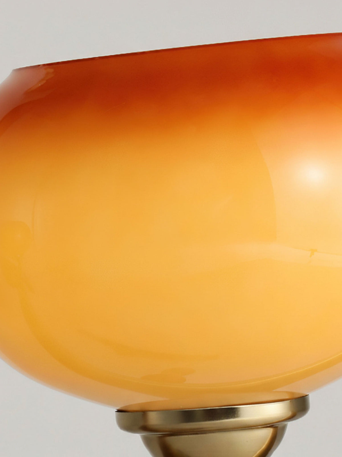 Close view of the glossy glass of a Clérachic shade, shading from golden yellow to deep orange, with the brass cap just visible below.