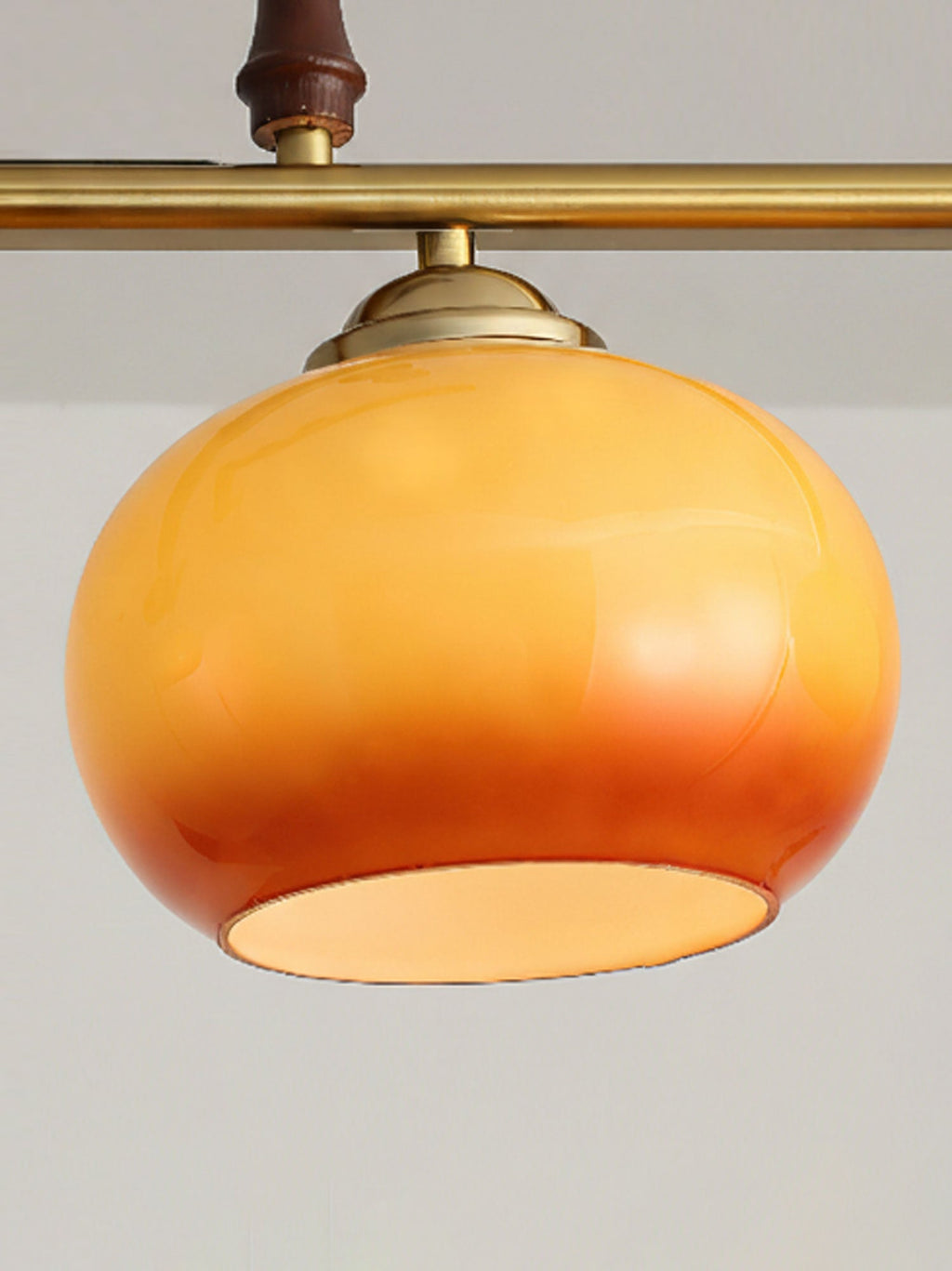 One round amber glass shade of this Clérachic pendant, with a brass cap and bar above and a wooden grip, its rim open at the base.