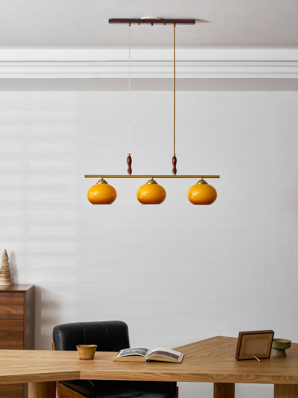 Clérachic three-head pendant on a long drop from a wooden ceiling plate, seen at a distance above a desk and a black leather chair.