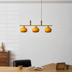 Wide shot of a Clérachic bar pendant with three amber shades, above a light wood desk with an open book and a small framed photo.