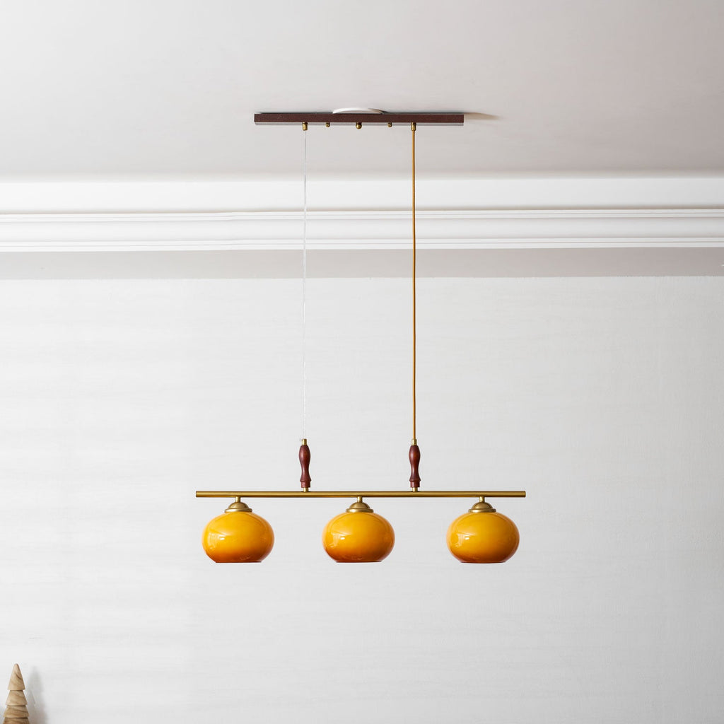 This Clérachic pendant hanging under a white cornice, its wooden canopy and three amber shades set against a pale panelled wall.