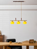 Lit amber shades of a Clérachic bar pendant in a bright room with white panelling, with a wooden desk and an open book below.