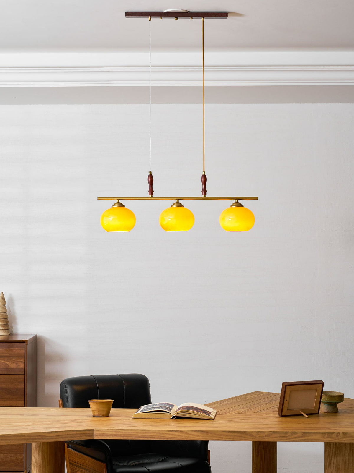Lit amber shades of a Clérachic bar pendant in a bright room with white panelling, with a wooden desk and an open book below.