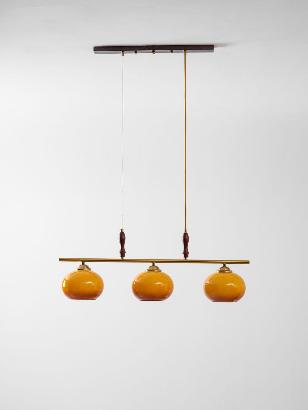 This Clérachic pendant on a plain white backdrop, with a dark wooden ceiling bar, two drop cords and three amber glass shades.