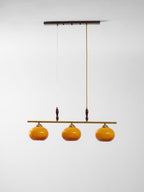 This Clérachic pendant on a plain white backdrop, with a dark wooden ceiling bar, two drop cords and three amber glass shades.