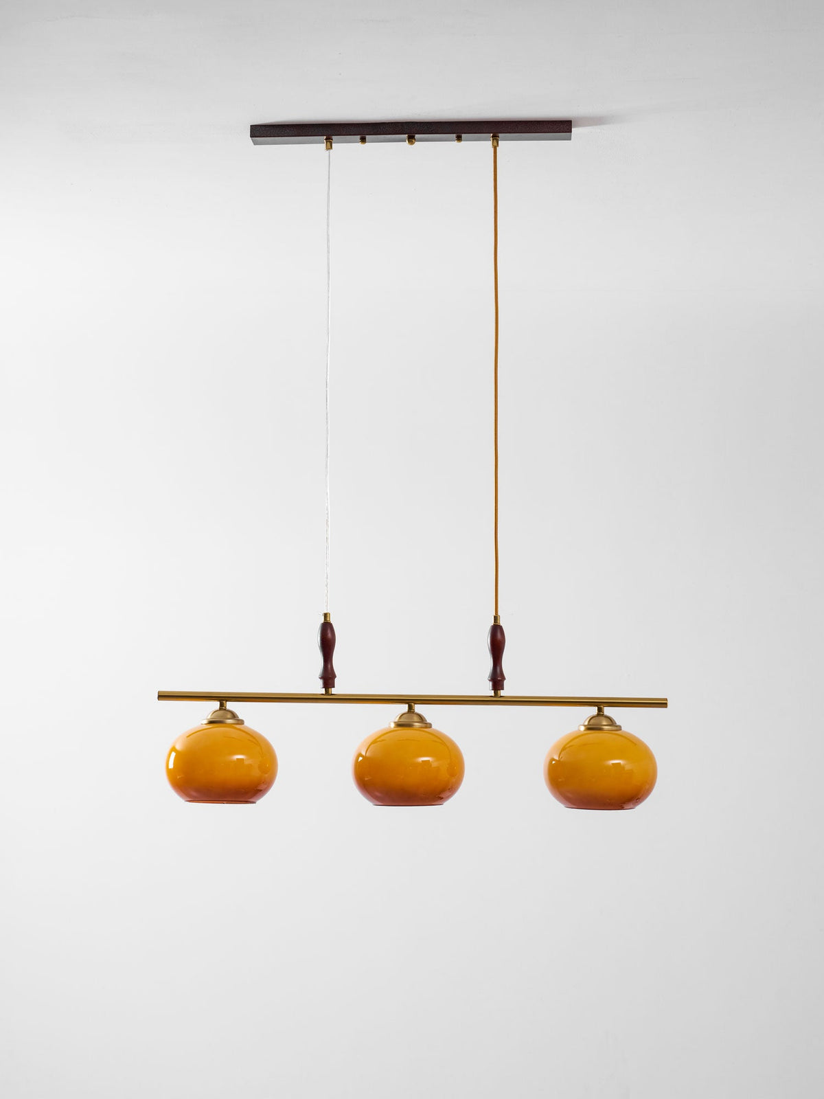 This Clérachic pendant on a plain white backdrop, with a dark wooden ceiling bar, two drop cords and three amber glass shades.
