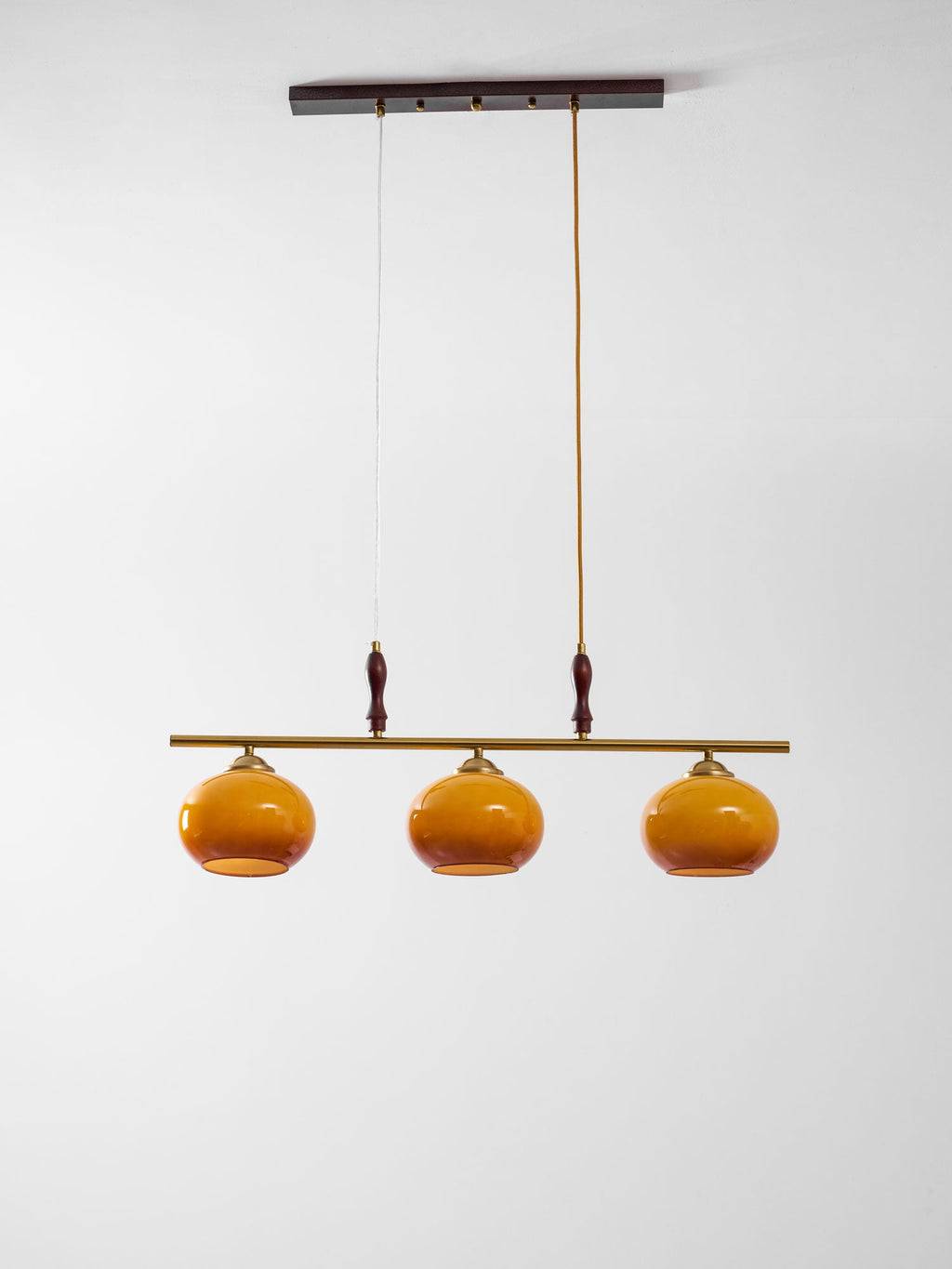 Full view of a Clérachic bar pendant from its dark ceiling plate to three small amber shades, on a soft grey-white backdrop.