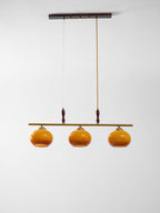 Full view of a Clérachic bar pendant from its dark ceiling plate to three small amber shades, on a soft grey-white backdrop.