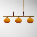 Brass bar of this Clérachic pendant with two turned wooden grips and three amber glass shades that darken towards the rim.