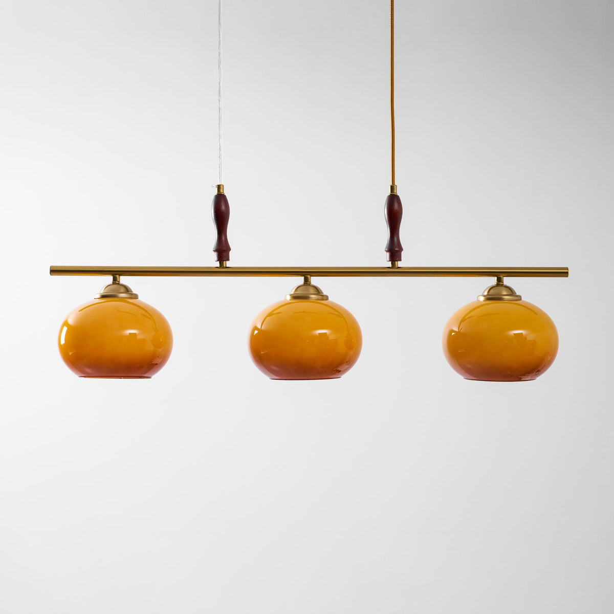 Brass bar of this Clérachic pendant with two turned wooden grips and three amber glass shades that darken towards the rim.
