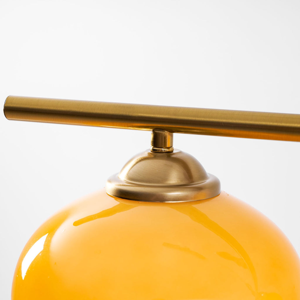 Close view of the brass bar, a domed brass cap and the glossy upper curve of an amber glass shade on this Clérachic pendant.