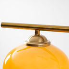 Close view of the brass bar, a domed brass cap and the glossy upper curve of an amber glass shade on this Clérachic pendant.