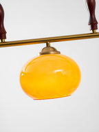 Single amber shade of this Clérachic pendant hung from a brass bar, with the dark turned wooden grips at the top edge of the frame.