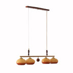 Four-head version of this Clérachic pendant on a white backdrop, with a wooden ceiling bar, a small wooden ball at the centre and amber shades.