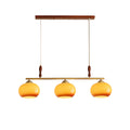 Three-head Clérachic pendant on a white backdrop, with a walnut-toned ceiling bar, brass bar, turned wooden grips and honey-amber glass shades.