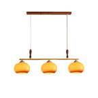 Three-head Clérachic pendant on a white backdrop, with a walnut-toned ceiling bar, brass bar, turned wooden grips and honey-amber glass shades.