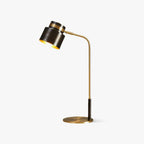 This Clérachic table lamp on a plain white backdrop, with a black drum shade, brass arm and round brass base.