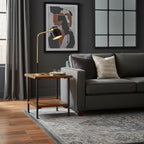 Beside a charcoal sofa, a Clérachic table lamp lights a small wood side table below abstract wall art and a grid mirror.