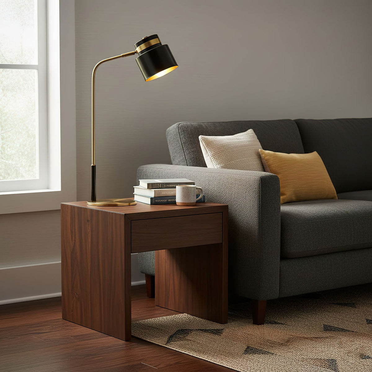 This Clérachic lamp stands on a walnut side table by a grey sofa, with a stack of books and a mug at its base.