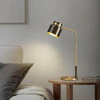 Lit softly beside a bed, a Clérachic table lamp rests on a round wooden table with a pair of glasses and a book.