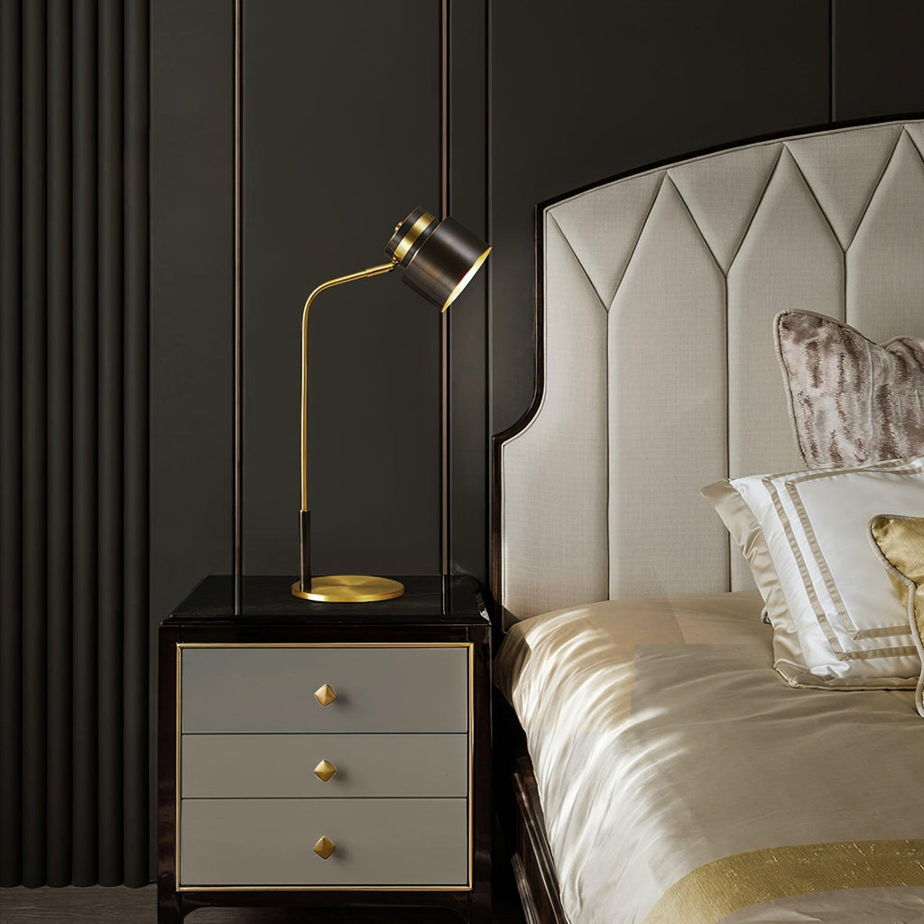 The Clérachic lamp on a black bedside chest with grey drawers, in front of a cream headboard and champagne bedding.