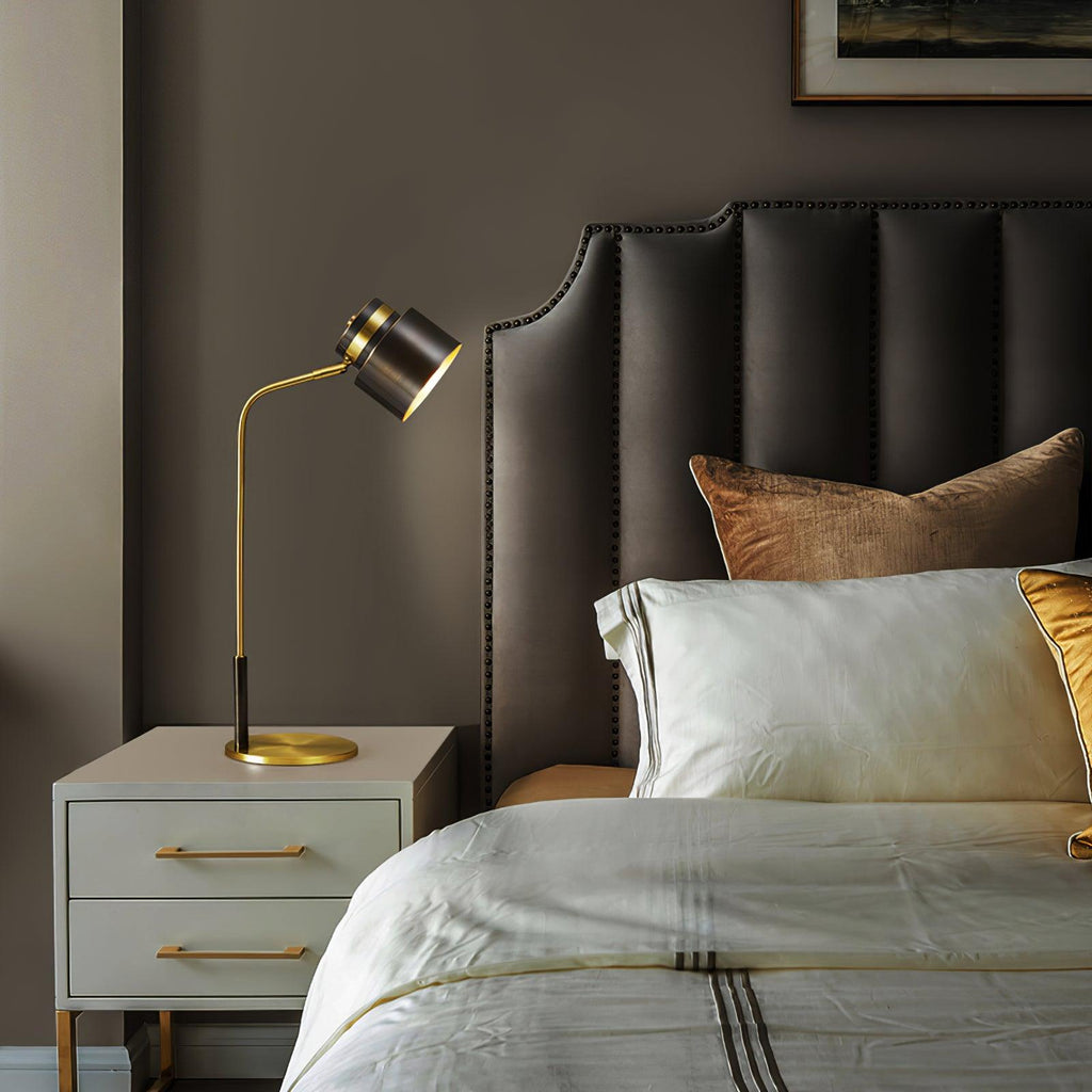 A Clérachic table lamp on a pale cabinet with brass pulls, with a padded taupe headboard and layered ivory bedding.