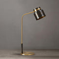 Close, straight-on view of this Clérachic table lamp on a grey backdrop, showing its dark shade, curved brass arm and round base.