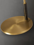 Close view of the round brushed-brass base and dark stem on this Clérachic table lamp, on a dark grey backdrop.