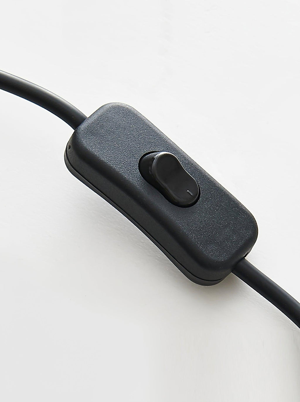 Close view of the black in-line push switch on the cord of this Clérachic table lamp, on a white surface.