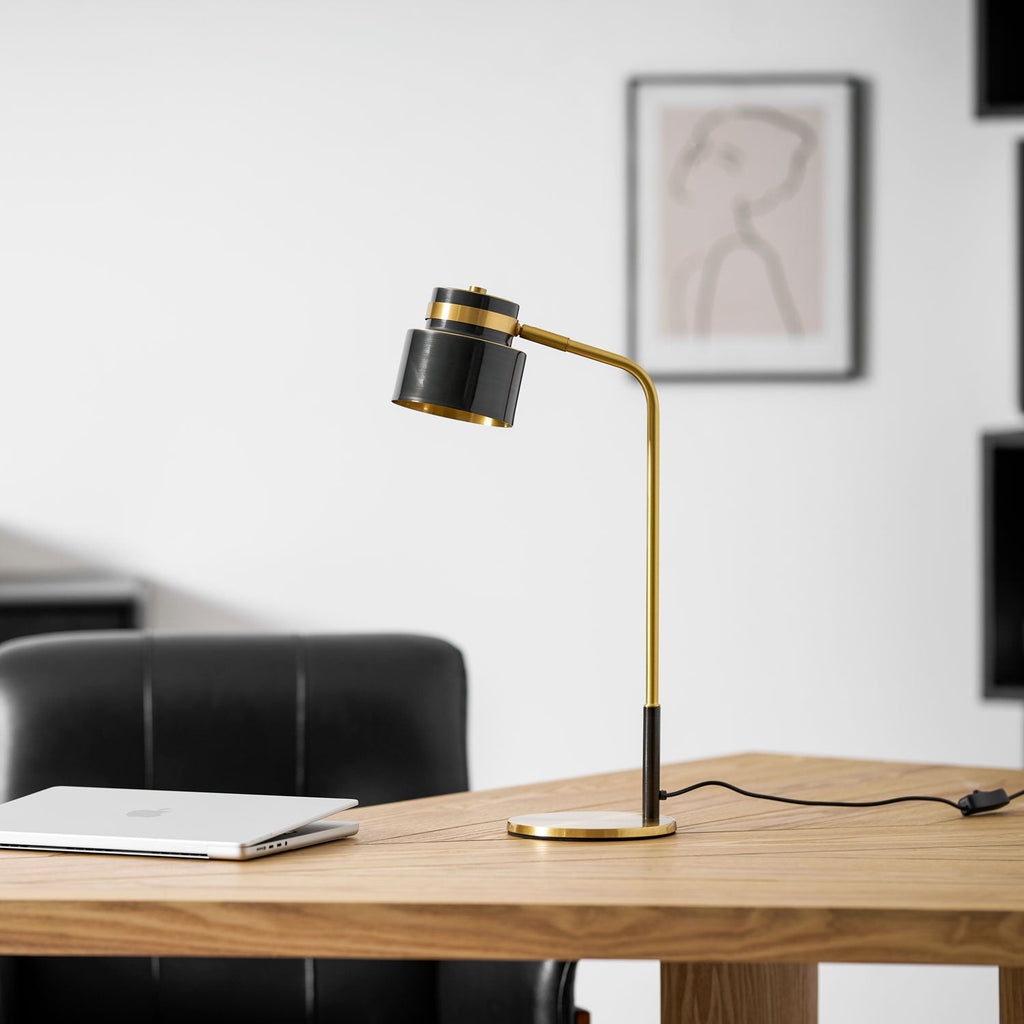 Seen from the left, a Clérachic table lamp on a wooden desk with its cord trailing to the right, a leather chair behind.