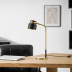 Seen from the left, a Clérachic table lamp on a wooden desk with its cord trailing to the right, a leather chair behind.