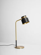A Clérachic table lamp on a pale grey surface, its black cord curving across the floor from the base.