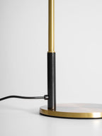 Close view of the base of this Clérachic table lamp, where the black cord enters beside the stem and brass disc.