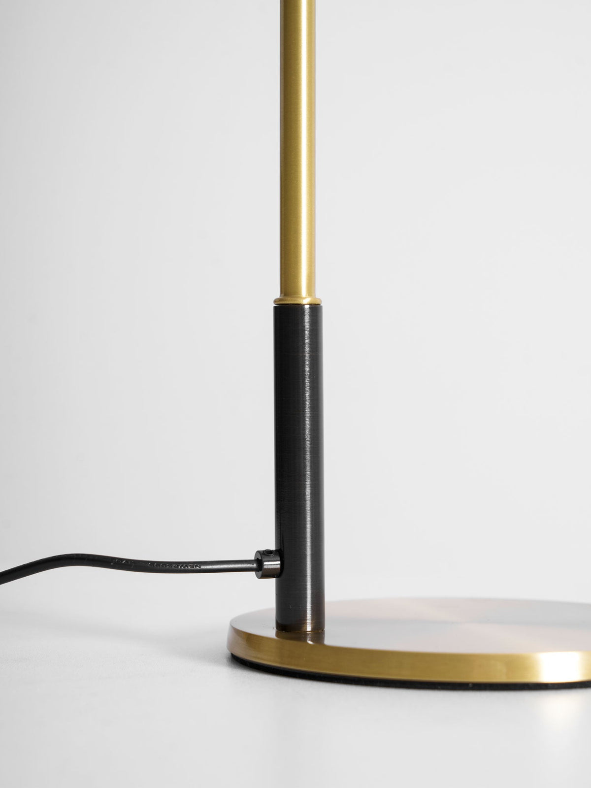 Close view of the base of this Clérachic table lamp, where the black cord enters beside the stem and brass disc.