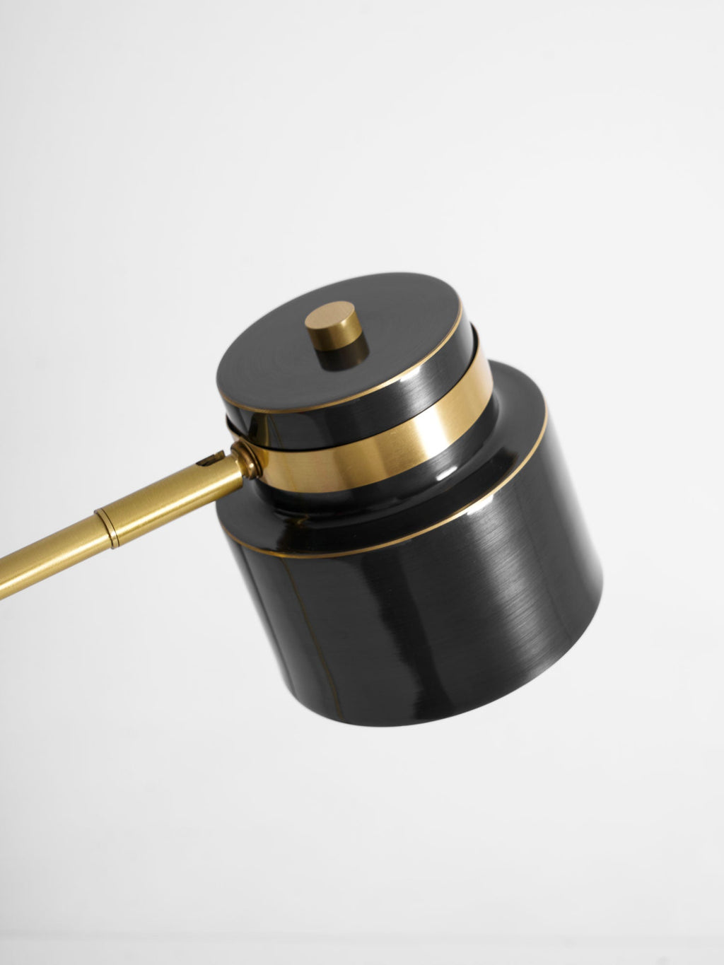Close view of the shade, brass band and arm joint on this Clérachic table lamp, tilted against a white backdrop.