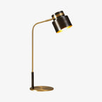 A Clérachic table lamp in close-up on a pale backdrop, with a dark shade, gold lining and a curved brass arm.