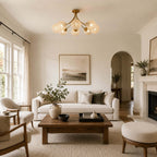 Brass bouquet Clérachic ceiling light over a living room with a linen sofa, a square wooden coffee table and an arched doorway.