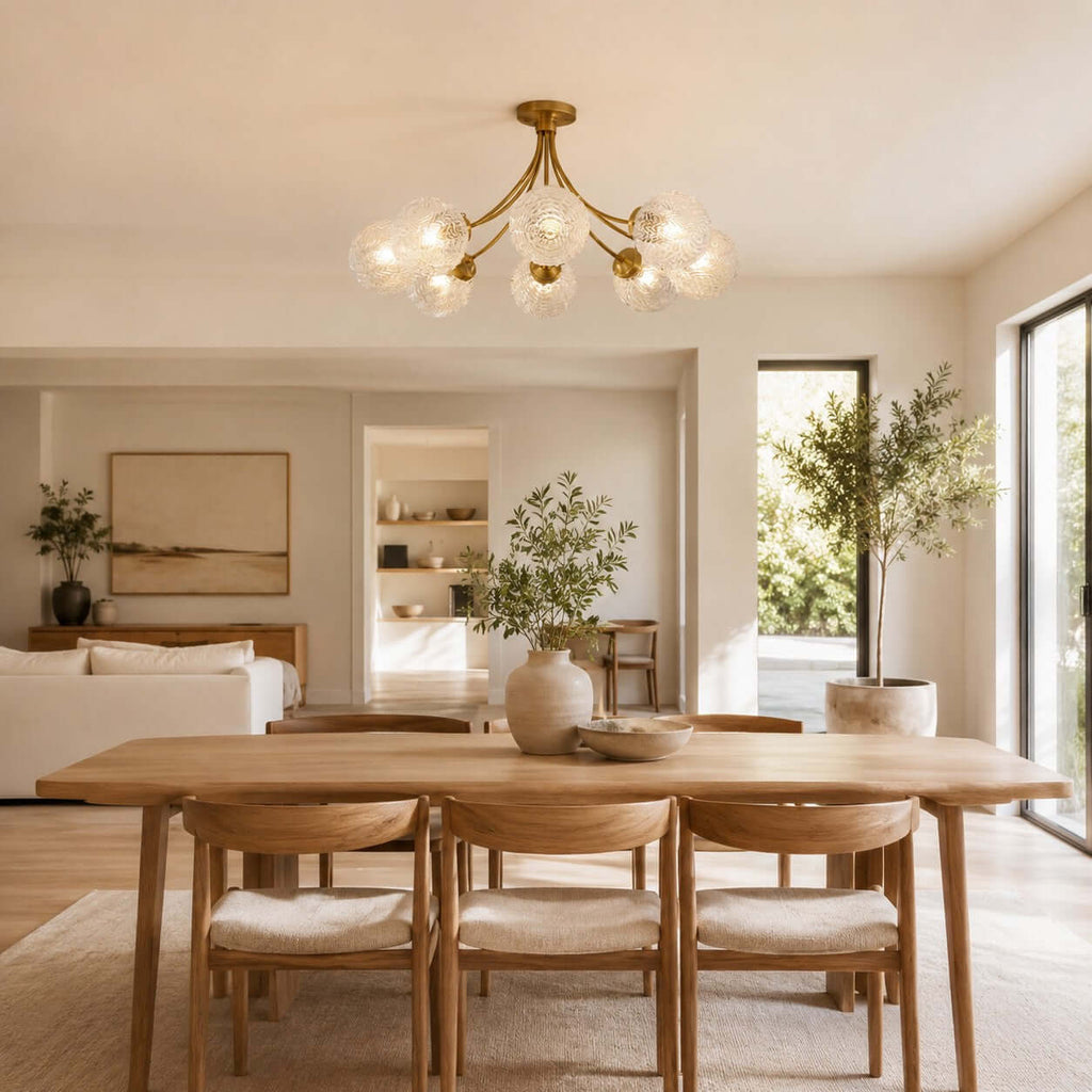 Clérachic brass ceiling light over a wooden dining table with cushioned chairs, in an open room with an olive tree.