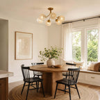 Clérachic ceiling light with rippled glass globes above a round wooden table and black spindle chairs, beside a window seat.