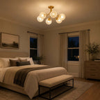 Clérachic ceiling light glowing in a dim evening bedroom with a bench at the bed foot and dark windows behind the curtains.