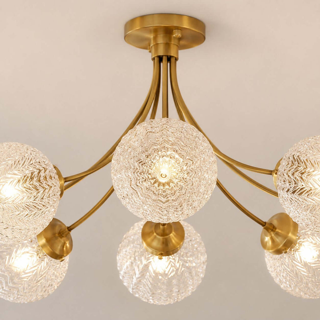 Close view of the rippled glass globes and brass arms of this Clérachic ceiling light, lit warm from below.