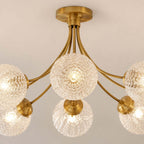 Close view of the rippled glass globes and brass arms of this Clérachic ceiling light, lit warm from below.