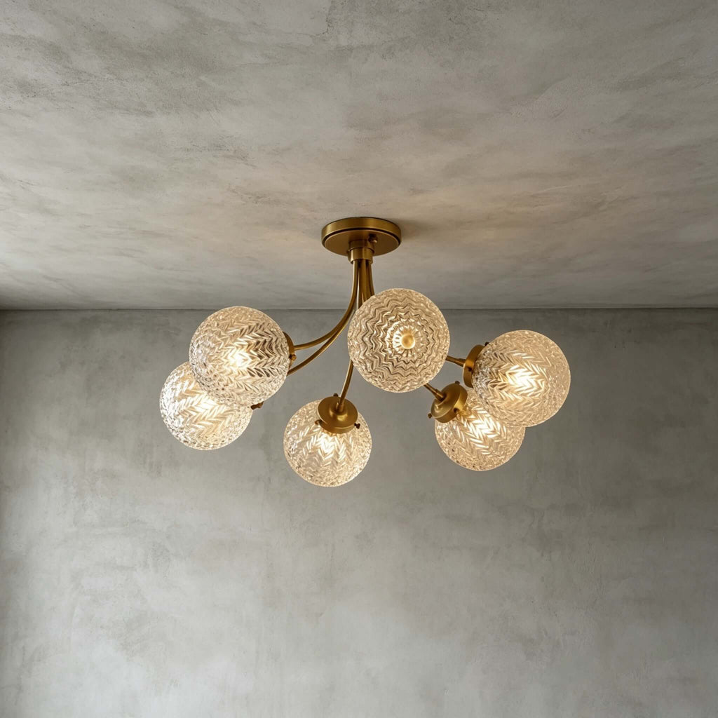 Five-globe Clérachic ceiling light with textured glass and brass arms, glowing on a grey plaster ceiling and wall.