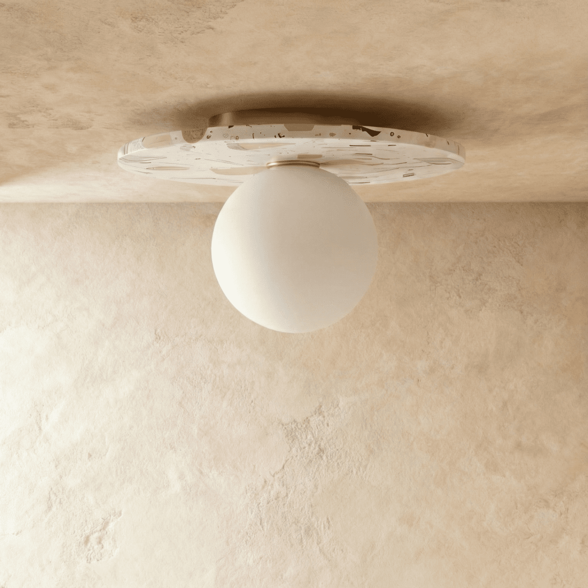 A terrazzo-disc ceiling light with an opal glass globe is shown unlit against a plain plaster ceiling, Clérachic hero shot.
