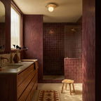 The terrazzo ceiling light glows above a burgundy-tiled walk-in shower and wood vanity in this Clérachic lifestyle shot.