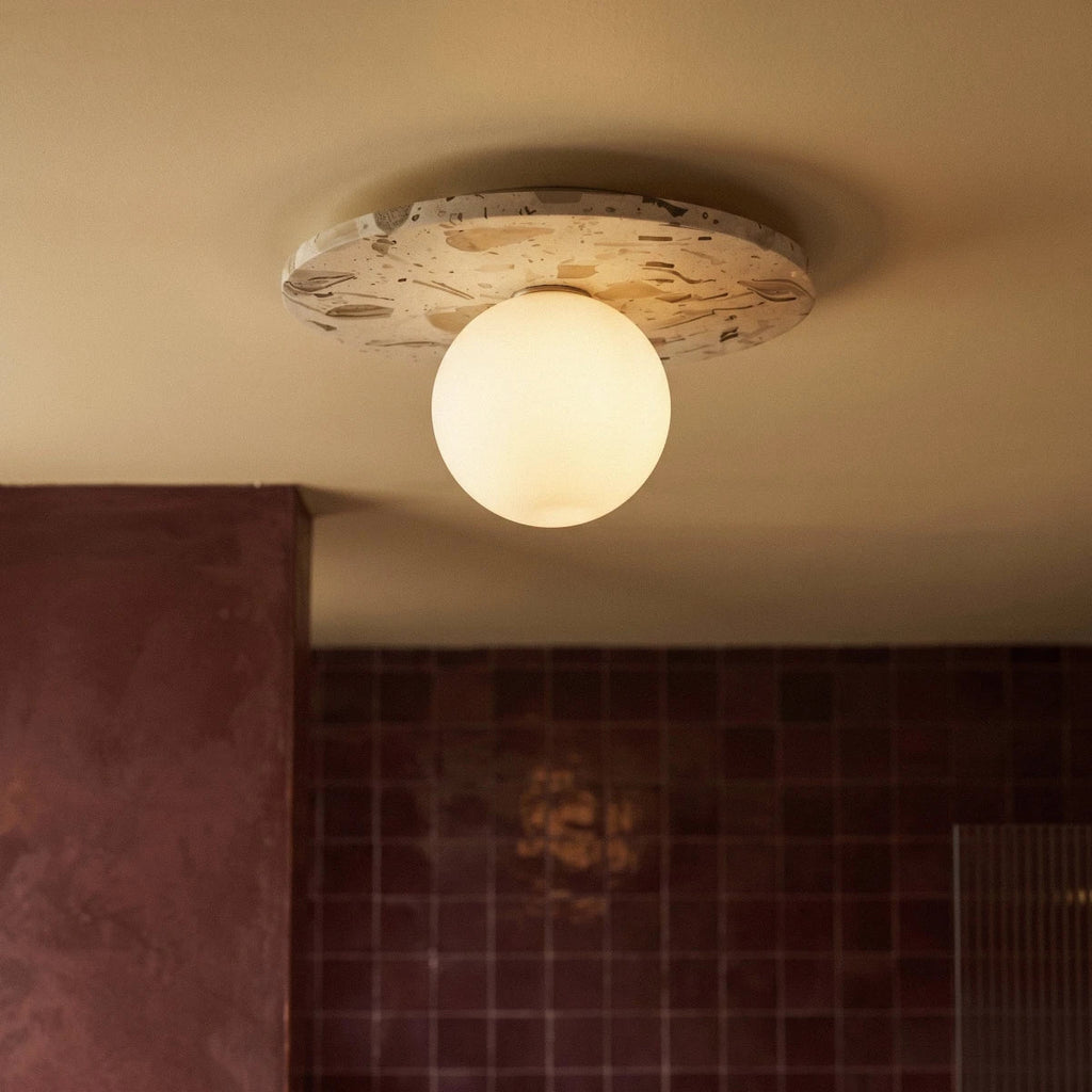 A closer crop shows the lit terrazzo ceiling light against burgundy tile and a plaster archway, Clérachic detail shot.