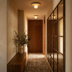 Two terrazzo ceiling lights glow along a wood-panelled hallway leading to a walnut door and mirror, Clérachic lifestyle shot.